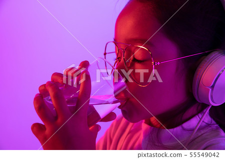Portrait of little girl in headphones on purple gradient background in neon light Portrait of little girl in headphones on purple gradient background in neon light 55549042