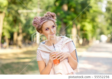 Young beautiful girl drinking fresh juice from plastic takeaway food cups after a walk outdoors Young beautiful girl drinking fresh juice from plastic takeaway food cups after a walk outdoors 55552256