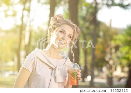 Young beautiful girl drinking fresh juice from plastic takeaway food cups after a walk outdoors 55552315