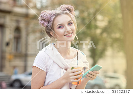 Happy smiling girl in pink sweatshirt with makeup and a bun of hair is sitting outside with a summer 55552327