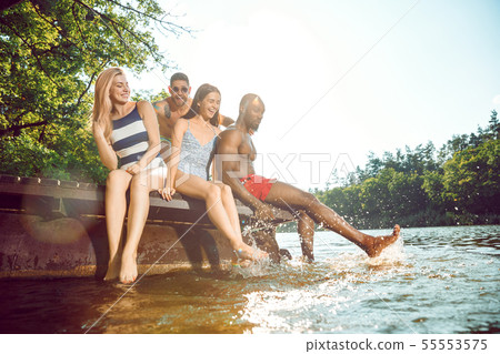 Group of happy friends having fun while sitting and laughting on the pier on river Group of happy friends having fun while sitting and laughting on the pier on river 55553575