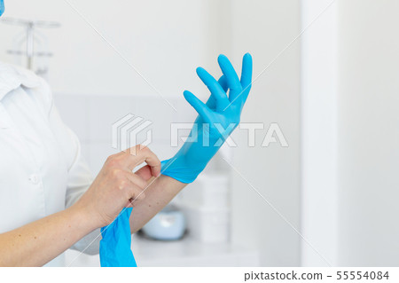 Nurse in scrub and mask puts gloves on her hands 55554084