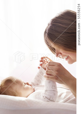 A newborn baby is lying on the bed and the mother is holding his hands 55556254