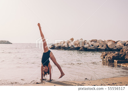 Active little girl at beach having a lot of fun. Cute kid making sporty exercises on the seashore Active little girl at beach having a lot of fun. Cute kid making sporty exercises on the seashore 55556517