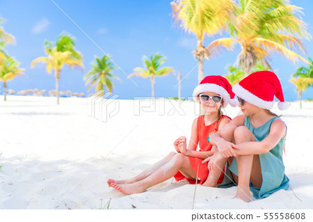 Little adorable girls in Santa hats during beach vacation have fun together Little adorable girls in Santa hats during beach vacation have fun together 55558608