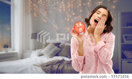 sleepy woman in pajama with alarm clock yawning 55571856