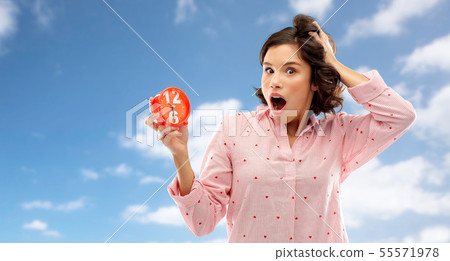 shocked young woman in pajama with alarm clock 55571978