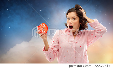 shocked young woman in pajama with alarm clock 55572617