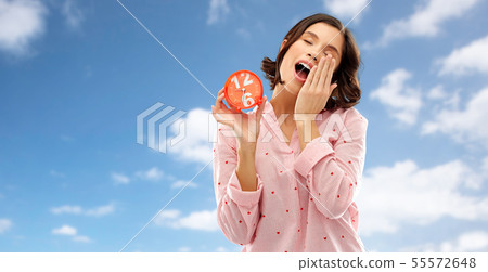 sleepy woman in pajama with alarm clock yawning 55572648