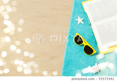 sunglasses and book on beach towel on sand 55573342