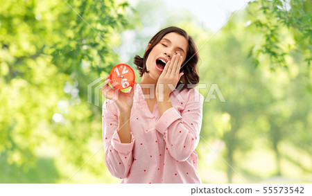 sleepy woman in pajama with alarm clock yawning 55573542