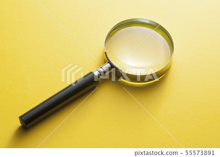 Magnifying glass lying diagonally on yellow 55573891