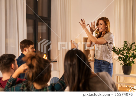 happy friends playing charades at home in evening 55574076