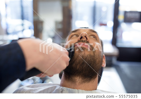 man and barber with trimmer cutting beard at salon man and barber with trimmer cutting beard at salon 55575035