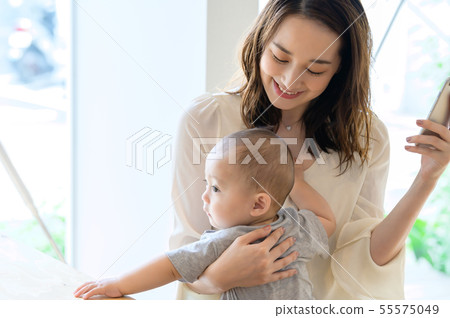 一個女人看著智能手機,同時抱著一個孩子 一個女人看著智能手機,同時抱著一個孩子 55575049