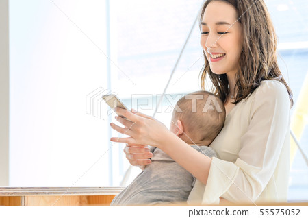 一個女人看著智能手機,同時抱著一個孩子 一個女人看著智能手機,同時抱著一個孩子 55575052