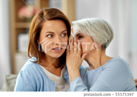 senior mother whispering to adult daughter at home 55575397