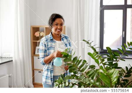happy woman spraying houseplant with water at home 55575654