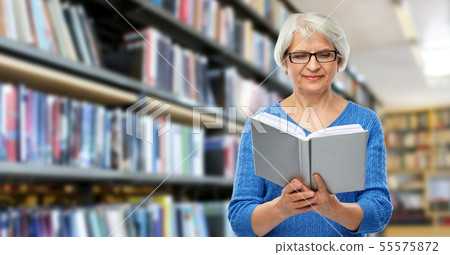 senior woman in glasses reading book at library 55575872