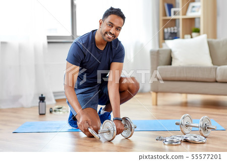smiling indian man assembling dumbbells at home smiling indian man assembling dumbbells at home 55577201