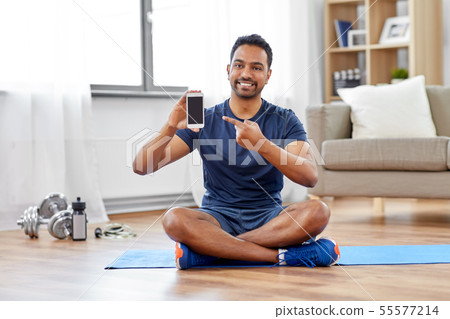 indian man with smartphone on exercise mat at home indian man with smartphone on exercise mat at home 55577214