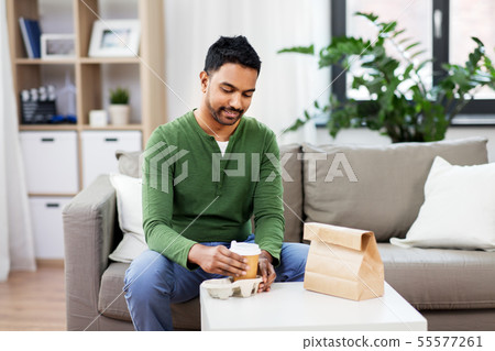 indian man with takeaway coffee and food at home 55577261