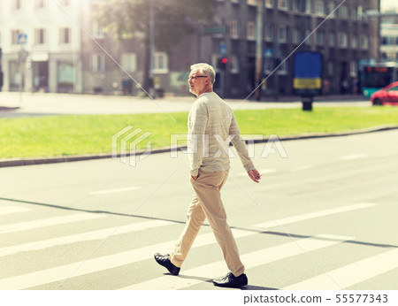 senior man walking along city crosswalk 55577343