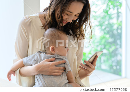 A woman who looks at a smartphone while holding a child A woman who looks at a smartphone while holding a child 55577968