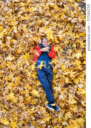Smiling blond boy lies strewn with yellow autumn Smiling blond boy lies strewn with yellow autumn 55584250