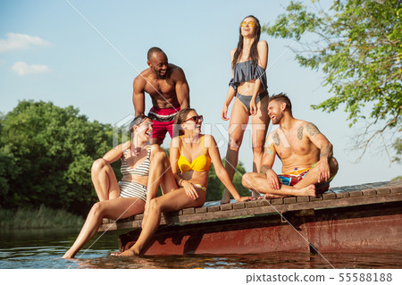 Group of friends splashing water and laughting on the pier on river 55588188