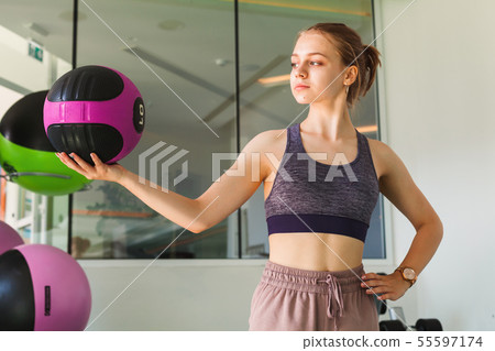 Blond sporty girl holds black pink med ball Blond sporty girl holds black pink med ball 55597174