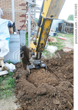 The excavator digs a small trench in the yard. The excavator digs a small trench in the yard. 55601485