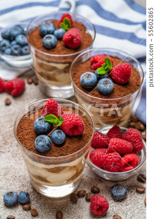 Classic tiramisu dessert with blueberries and raspberries in a glass and napkin on concrete Classic tiramisu dessert with blueberries and raspberries in a glass and napkin on concrete 55602865