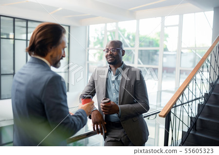 Bearded dark-skinned man wearing glasses speaking with colleague Bearded dark-skinned man wearing glasses speaking with colleague 55605323