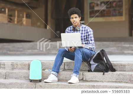 Handsome black teen sitting on stairs with laptop Handsome black teen sitting on stairs with laptop 55605383