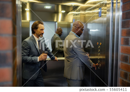 Man pressing button in elevator while standing near colleague 55605411