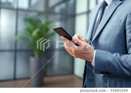 Close up of businessman wearing grey suit holding black smartphone Close up of businessman wearing grey suit holding black smartphone 55605504