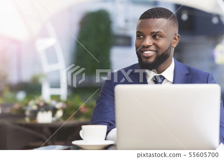 Afro Businessman Working On Laptop Having Coffee In Outdoor Cafe Afro Businessman Working On Laptop Having Coffee In Outdoor Cafe 55605700