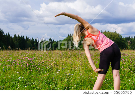 young woman doing exercises stretching in a meadow young woman doing exercises stretching in a meadow 55605790
