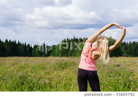 young woman doing exercises stretching in a meadow young woman doing exercises stretching in a meadow 55605792
