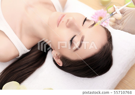 Close up of hands of expert beautician injecting in female forehead. The woman closed her eyes with 55710768