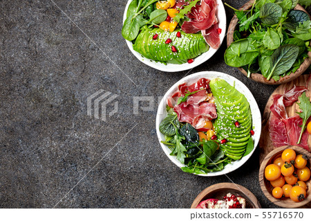 Low carbs bowl. Fresh salad with green spinach, rucola, avocado an ham serrano in white bowl, gray 55716570