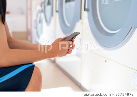 Coin laundry Men who wait while playing with their smartphone Coin laundry Men who wait while playing with their smartphone 55734972