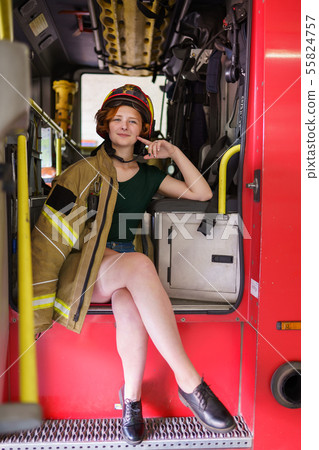 Image of ginger firewoman in helmet looking in camera sitting in cab of fire engine Image of ginger firewoman in helmet looking in camera sitting in cab of fire engine 55824757