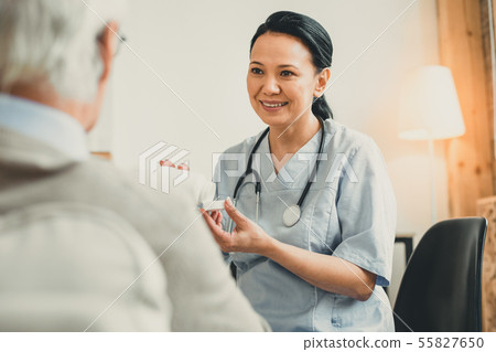 Cheerful dark-haired doctor presenting new medicines to her patient 55827650