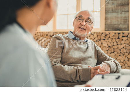 Confident pleasant old man sitting with windows behind 55828124