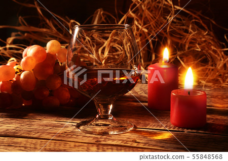 glass with cognac or whisky, grapes and christmas candles on wood background. Christmas decoration. 55848568