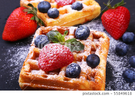 Homemade Traditional belgian waffles with fresh fruit, berries and sugar powder on black plate. Homemade Traditional belgian waffles with fresh fruit, berries and sugar powder on black plate. 55849618