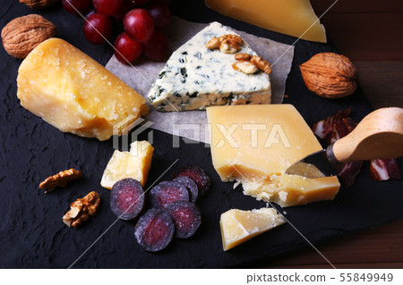 Assortment of cheese with fruits, grapes, nuts and cheese knife on a wooden serving tray. Assortment of cheese with fruits, grapes, nuts and cheese knife on a wooden serving tray. 55849949
