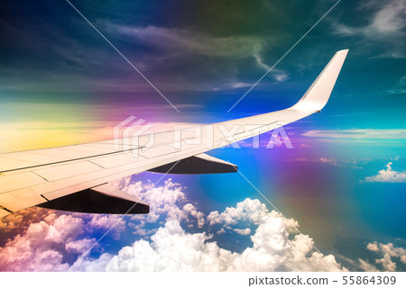 Wing of airplane in cloudy sky with rainbow effect 55864309